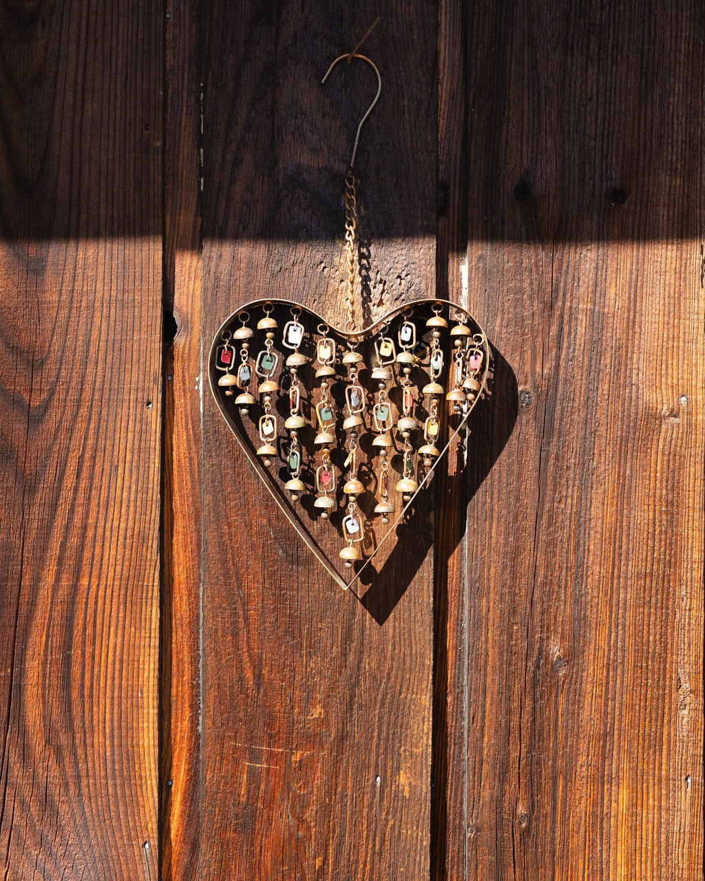 Brass heart-shaped wind chime with hanging strands of small bells and colorful enamel tags, suspended by a chain