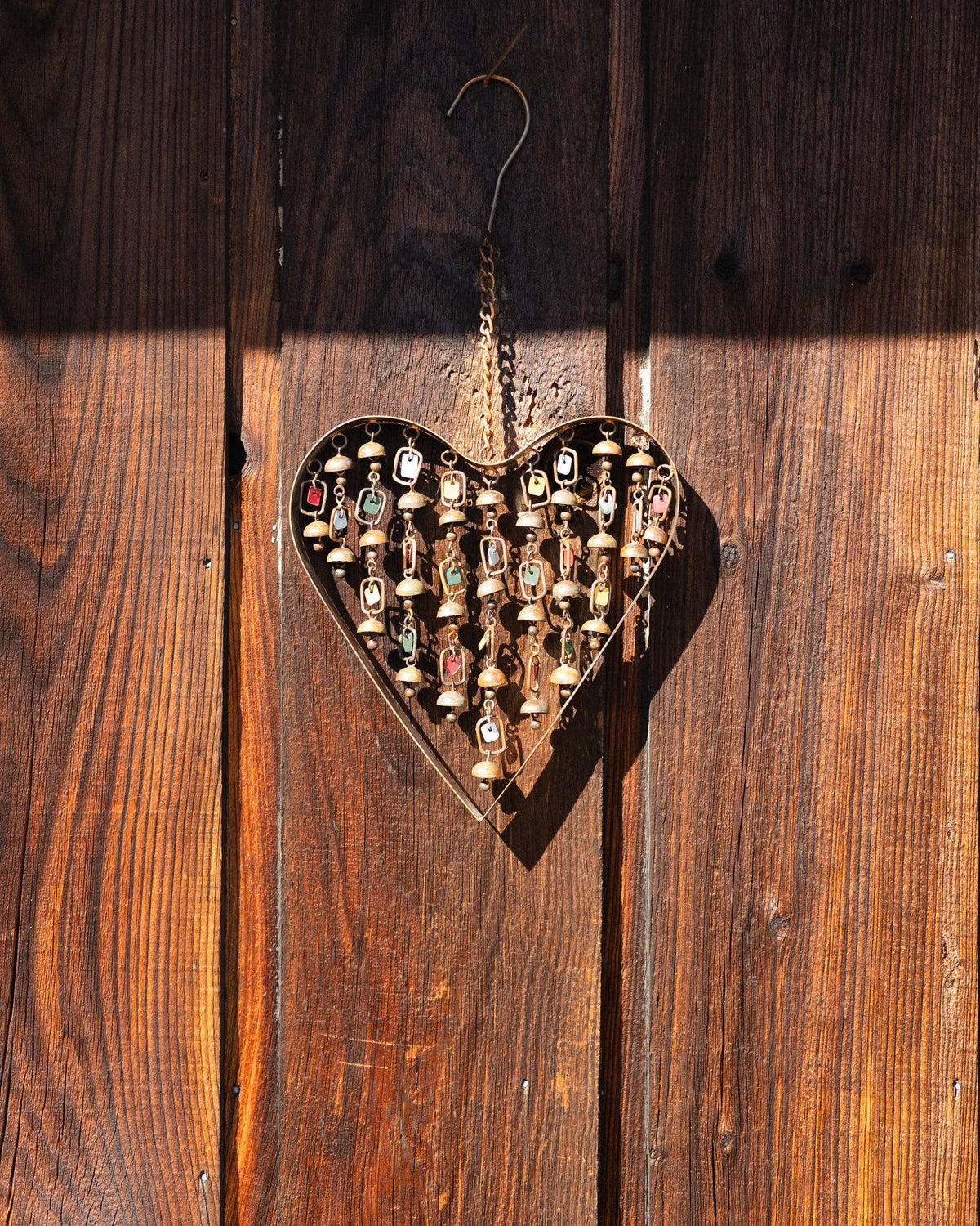 Brass heart-shaped wind chime with hanging strands of small bells and colorful enamel tags, suspended by a chain